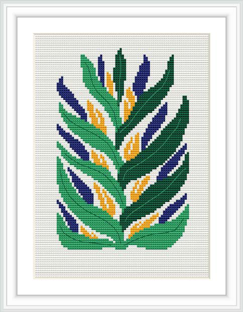 The image depicts a framed cross stitch pattern featuring stylized tropical leaves arranged in a symmetric composition. The leaves are stitched in various shades of green, with accents in yellow and blue, against a white background.