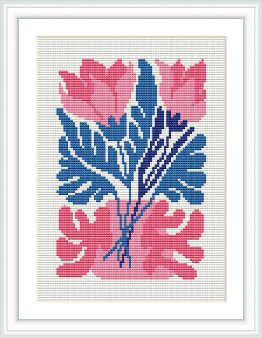 The image displays a cross stitch pattern featuring a bouquet of stylized flowers primarily in shades of pink and blue, with a white background. It appears to be framed and is possibly meant to be used as wall art or home decor.