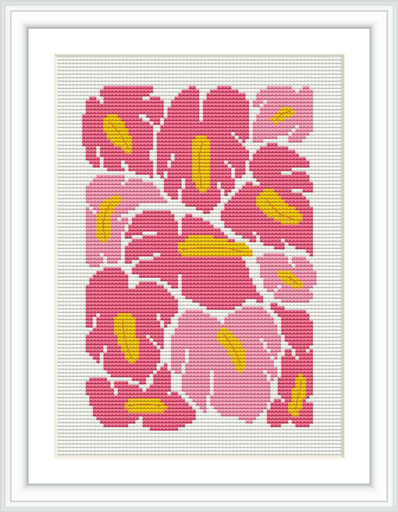 The image depicts a framed cross stitch pattern featuring a design of pink and yellow leaves on a stark white background, encased within a simple white frame.