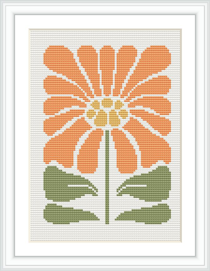 The image displays a framed cross stitch pattern of an orange flower with a central yellow core and green leaves, set against a white background.