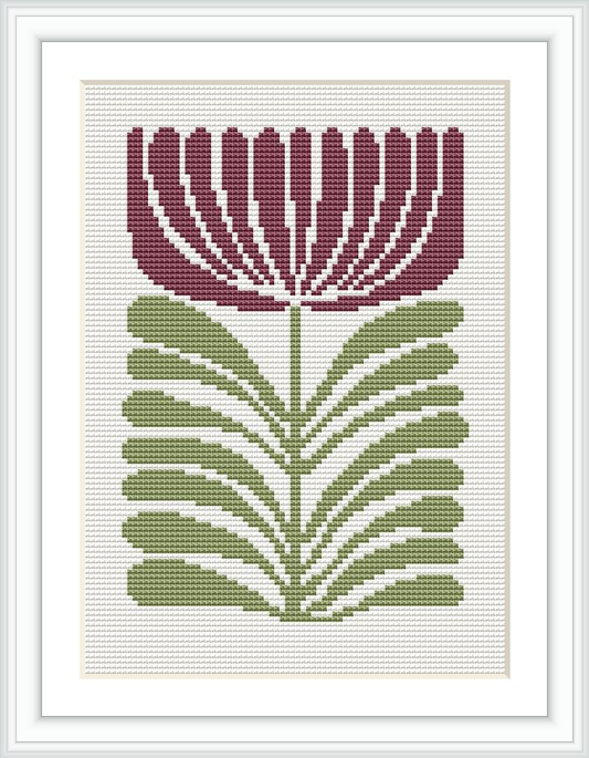 The image shows a framed cross stitch embroidery of a stylized flower with maroon petals and green leaves, centered on a white canvas.