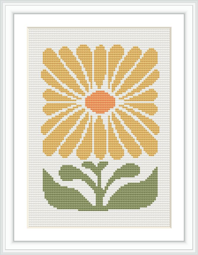 The image shows a framed cross stitch pattern featuring a stylized yellow flower with a central orange disc, surrounded by petals, sitting above two green leaves. The background is white.