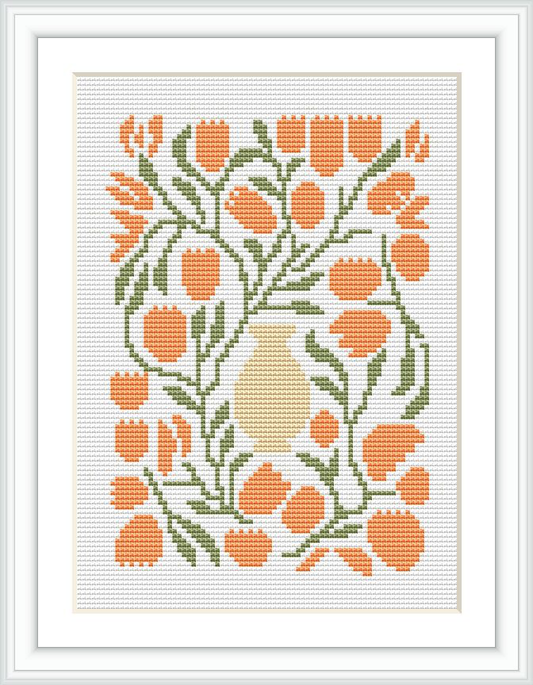 The image shows a cross stitch pattern of a cream-colored vase with a bouquet of orange tulips surrounded by green foliage, encased within a white border and framed.