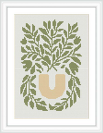 The cross stitch pattern features a collection of leafy branches in various shades of green, emanating from a simple, beige-colored vase at the center of a white canvas.