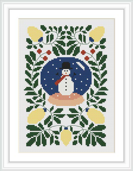 The image showcases a cross stitch pattern comprising a central snowman encircled by a dark blue background, framed by a symmetrical arrangement of green leaves, red berries, and yellow candle-like motifs on a white fabric, all within a decoratively patterned border.