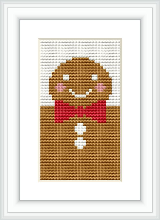 The image features a framed cross stitch pattern of a smiling gingerbread man with cheeks, eyes, and a bow tie in red and pink, centered on a piece of fabric.