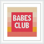 The image displays a framed cross stitch pattern featuring the phrase 'BABES CLUB' in block capital letters centered on a red background with a top and bottom border of yellow, pink, and beige stripes.