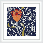 A cross stitch pattern featuring a single tulip in an array of rust orange with a navy blue background, surrounded by white botanical patterns and framed in a simple white border inside a dark frame.