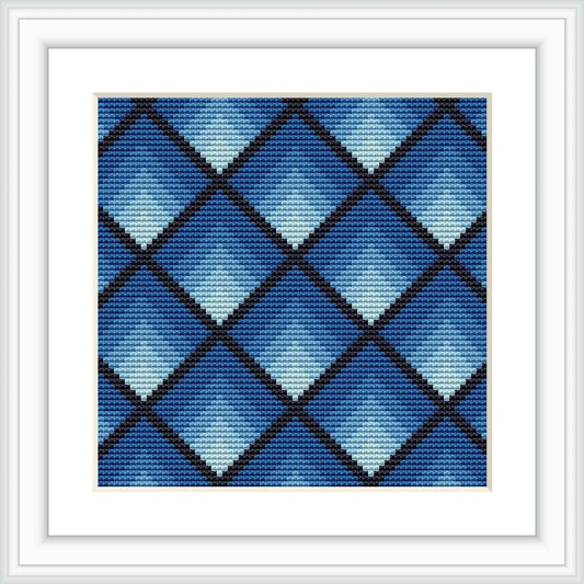 The image shows a framed cross stitch pattern featuring a geometric diamond design. The diamonds are arranged in a grid, varying in shades of blue, and are contained within a white square frame.