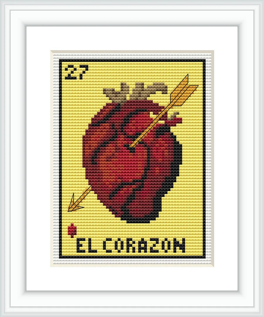 The image depicts a framed cross stitch pattern featuring a red heart with yellow highlights and embellished with two arrows. The background is cream-colored, and the text 'El Corazon' is stitched at the bottom along with the number 27 at the top, mimicking a Lotería card.