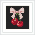 The image depicts two red cherries with attached green stems, tied together by a pink bow, centered on a black background within a white square frame.